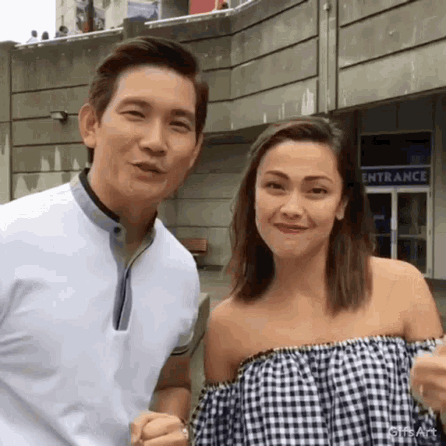 a man and a woman are posing for a picture in front of a building that says entrance