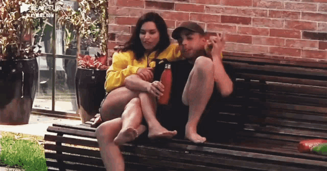 a man and a woman are sitting on a wooden bench in front of a brick wall and the website playeup.com