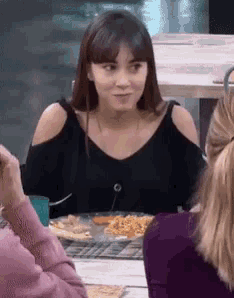 a woman in a black off the shoulder top is sitting at a table with other people .