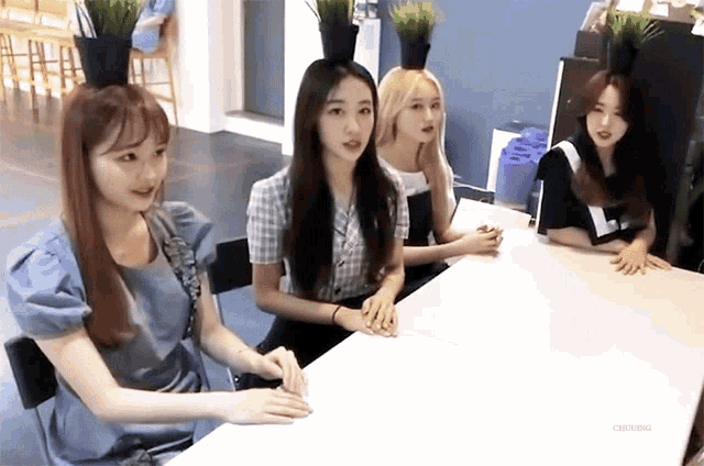 a group of young women sitting at a table with potted plants on their heads