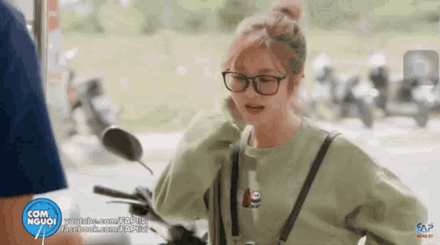 a woman wearing glasses and a green shirt with a bear on it is riding a motorcycle