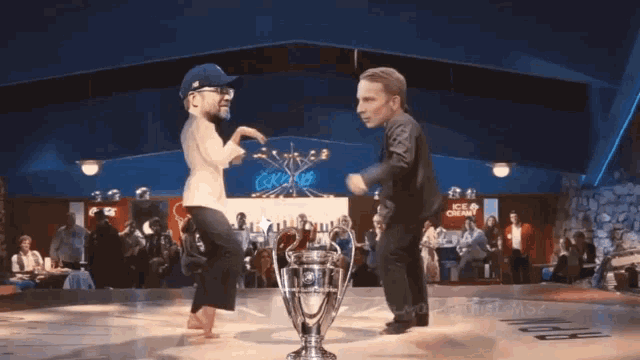 two men are dancing in front of a trophy with a sign that says ice cream in the background