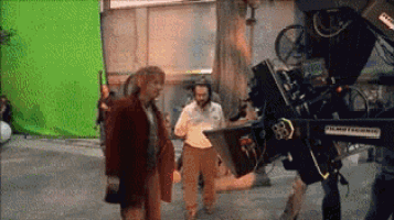 two men are standing in front of a green screen while a cameraman takes a picture