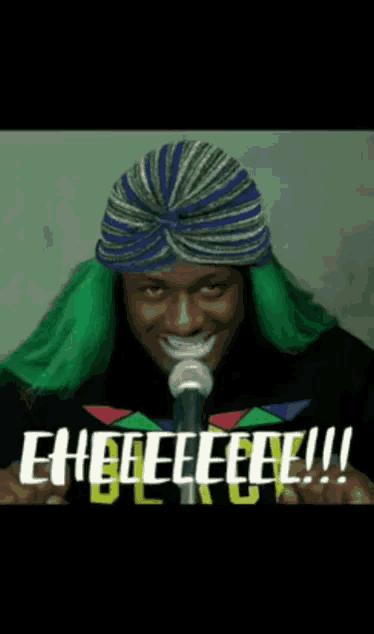 a man with green hair is smiling in front of a microphone with the words ehbeeee written on the bottom