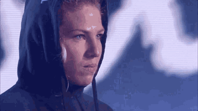 a woman wearing a black hoodie with a hood on her head is looking at the camera .