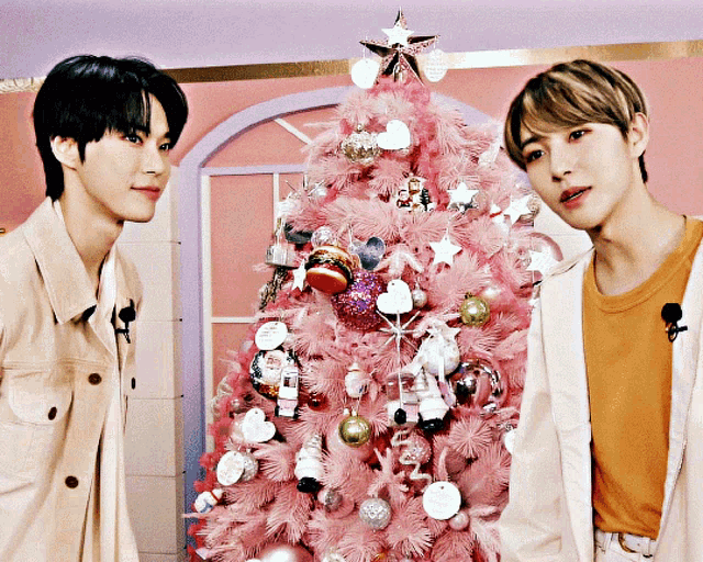 two men standing next to a pink christmas tree