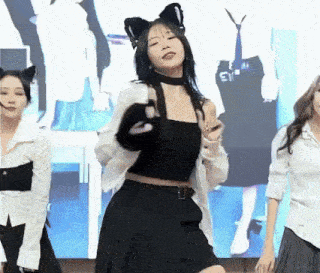 a woman wearing cat ears and a choker is dancing in front of a large screen