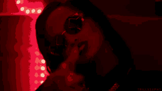 a woman wearing sunglasses in a dark room with red lights .