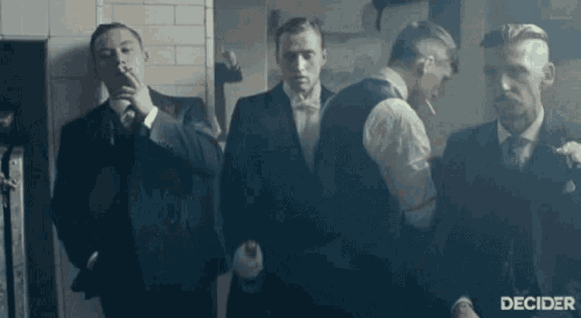 a group of men in suits and bow ties are standing next to each other smoking cigarettes .