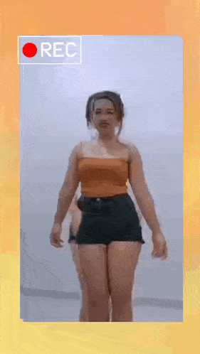 a woman in a tank top and shorts is standing in front of a camera with the word rec on it .