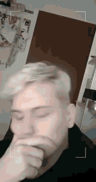 a young man with blonde hair is covering his mouth with his hand in a kitchen .