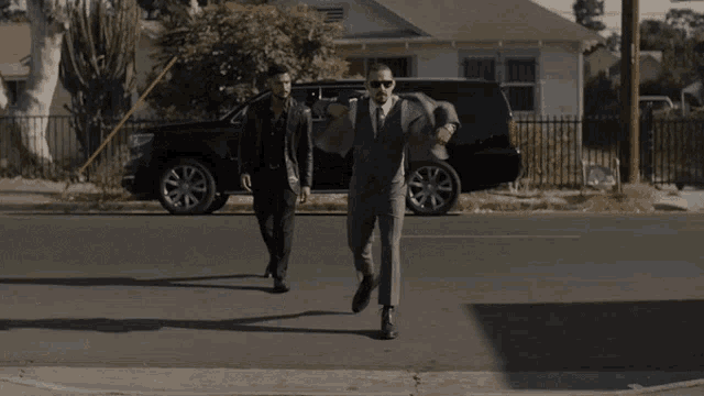 two men in suits are walking down a sidewalk
