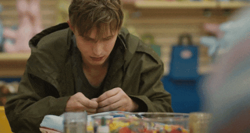 a man in a green jacket is sitting at a table with a bowl of candy in front of him