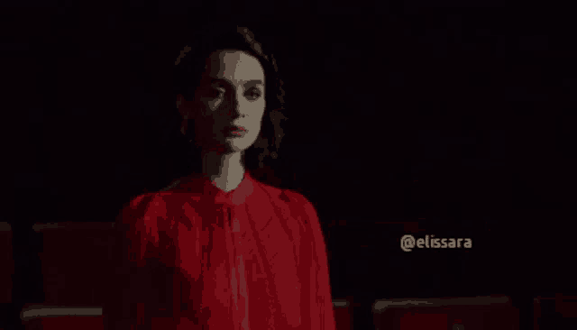 a woman in a red dress is standing in a dark room in front of red seats .