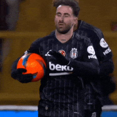 a soccer player wearing a beko jersey holds an orange ball