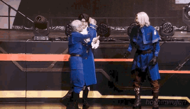 a group of people in blue uniforms are dancing on a stage with the name hoshimiruji on the bottom right corner
