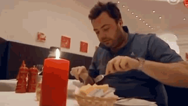 a man is sitting at a table with a candle in front of him eating .