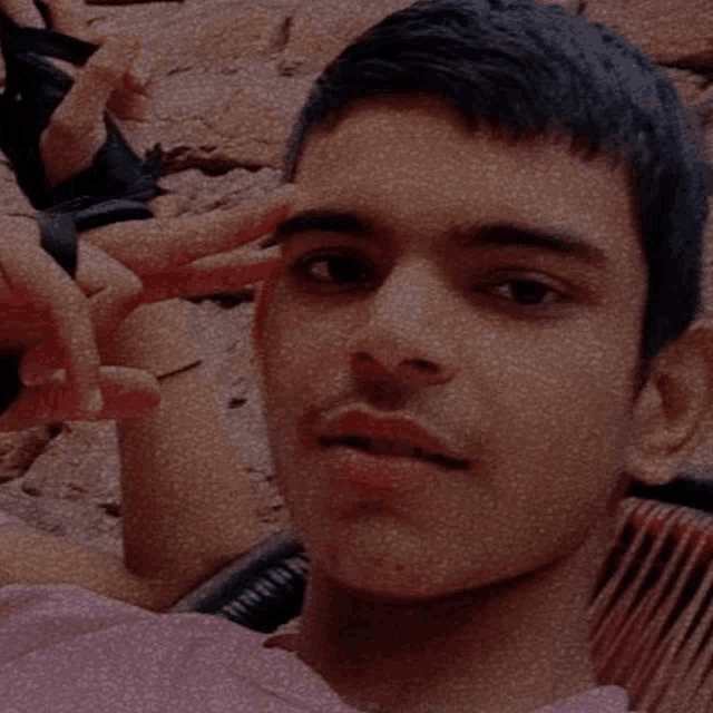 a young man in a pink shirt is giving a peace sign