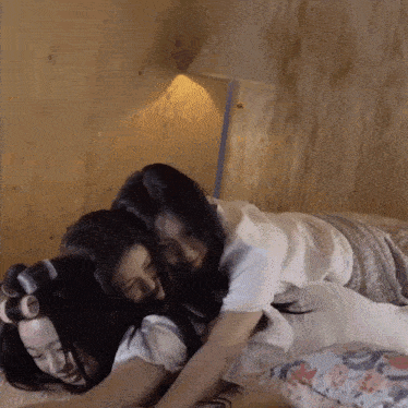 three women are laying on a bed with a lamp behind them