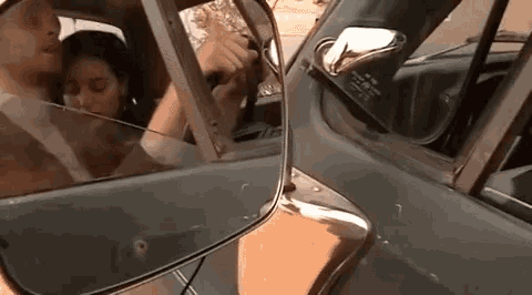 a man and a woman are kissing in a car while looking at each other in the rear view mirror .