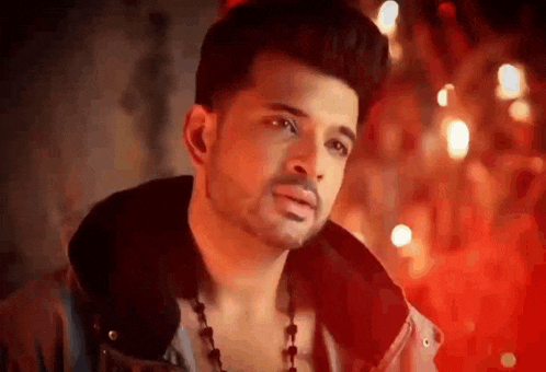 a man wearing a jacket and a necklace is looking at the camera .