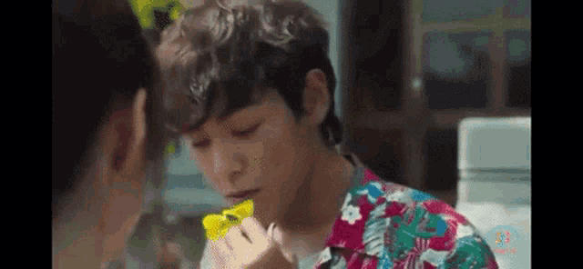 a young man in a colorful shirt is eating a yellow flower while a woman looks on .