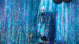 a person standing in front of a blue curtain with tinsel hanging from it .