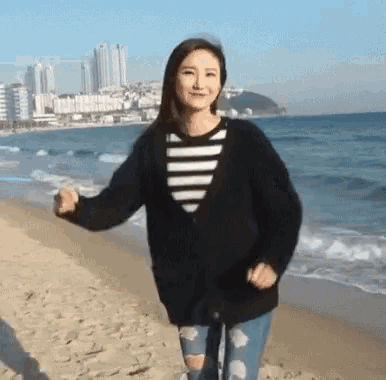a woman is standing on a beach with her arms outstretched and a city in the background .