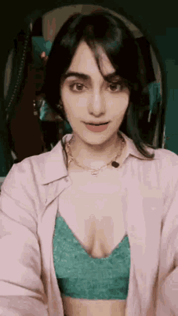 the woman is wearing a pink shirt and a green bra and taking a selfie .