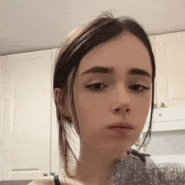a young woman is making a funny face in front of a kitchen cabinet .