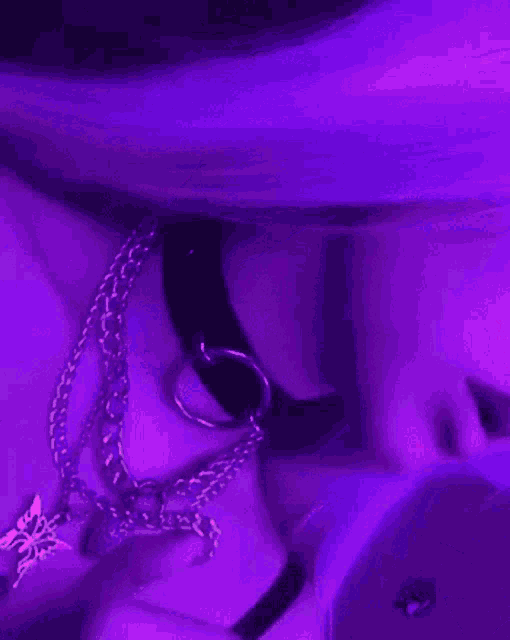 a close up of a person wearing a choker and necklaces in a purple light .