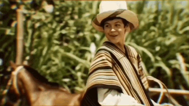 a man wearing a hat and a poncho is riding a horse