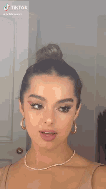 a woman is taking a selfie in front of a mirror while wearing a bun and a necklace .