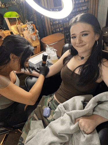 a woman is getting a tattoo on another woman 's arm and smiling