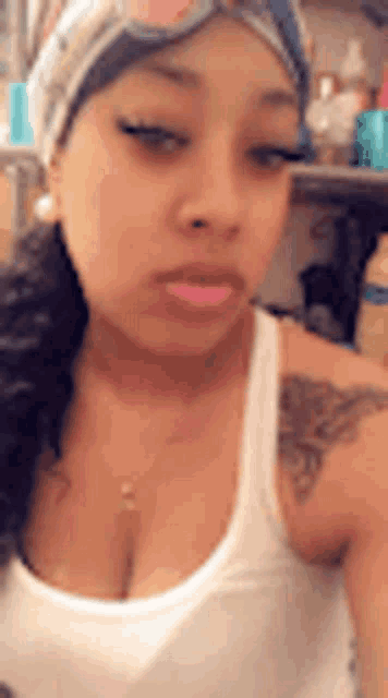 a woman wearing a white tank top and sunglasses is taking a selfie .