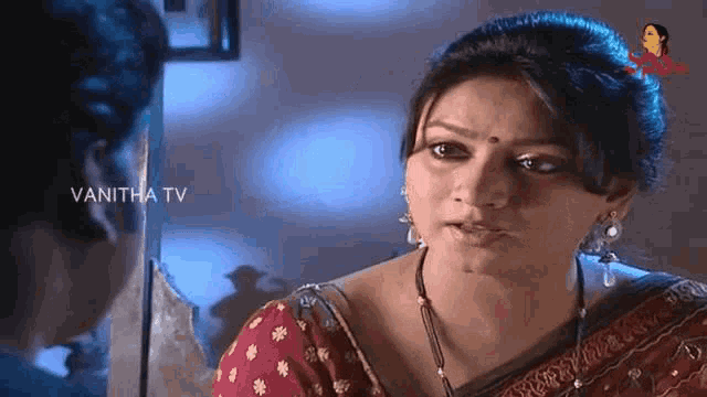 a woman in a red saree is looking at a man in a mirror .