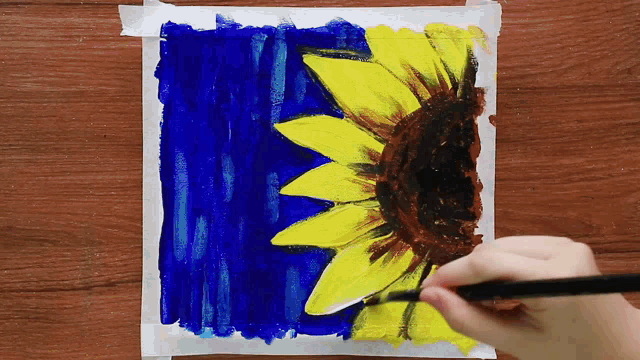 a person is painting a sunflower with a blue background