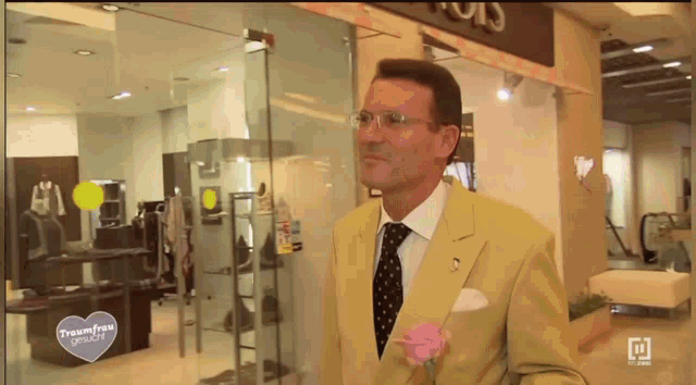 a man in a yellow suit and tie stands in front of a store with a sign that says teamfree gerade