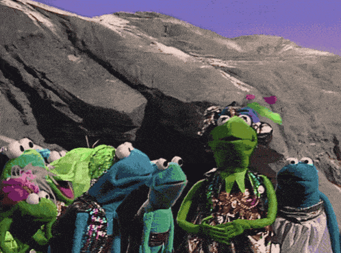 a group of stuffed frogs standing in front of a mountain