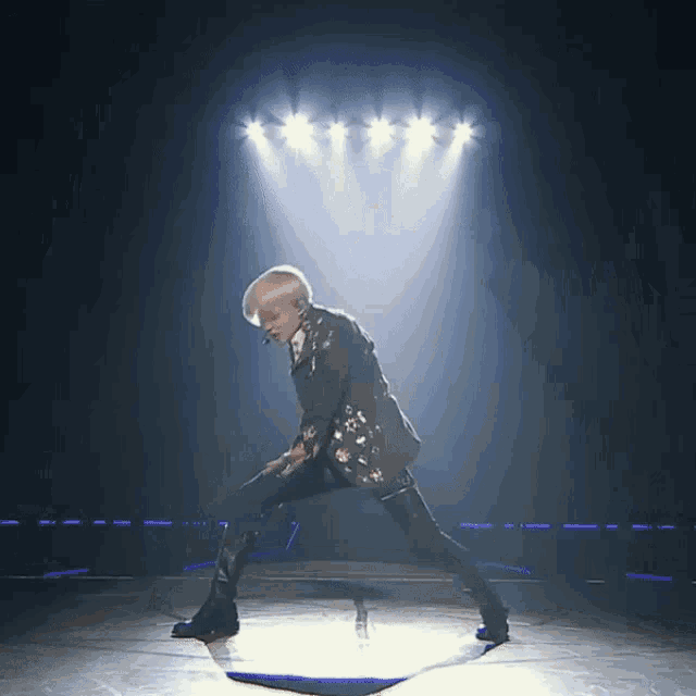 a man in a suit is dancing on a stage in front of a row of lights