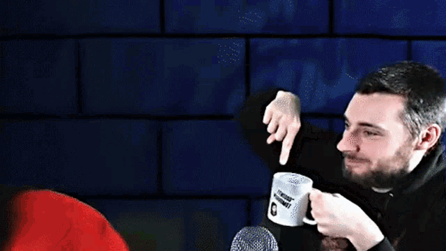 a man with a beard is pointing at something while holding a coffee mug that says jtm666f