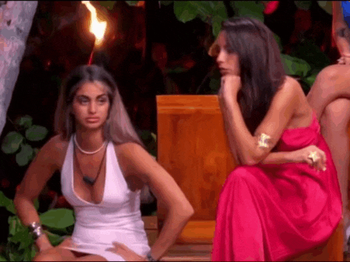 two women in dresses are sitting next to each other on a bench .