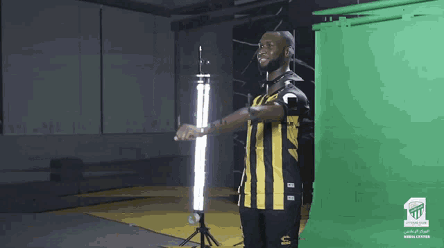 a man in a black and yellow striped shirt stands in front of a green screen with the letters t on it