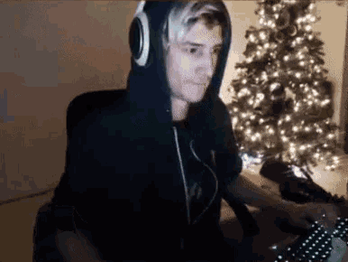 a man in a black hoodie is sitting in front of a christmas tree .