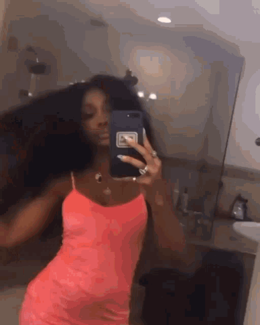 a woman in a pink dress is taking a picture of herself in a bathroom mirror .