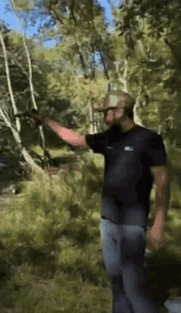 a man in a black t-shirt is holding a gun in a forest