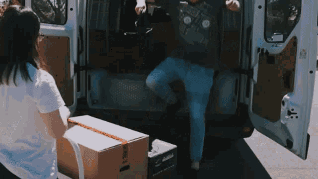 a man and a woman are loading boxes into a van with the door open