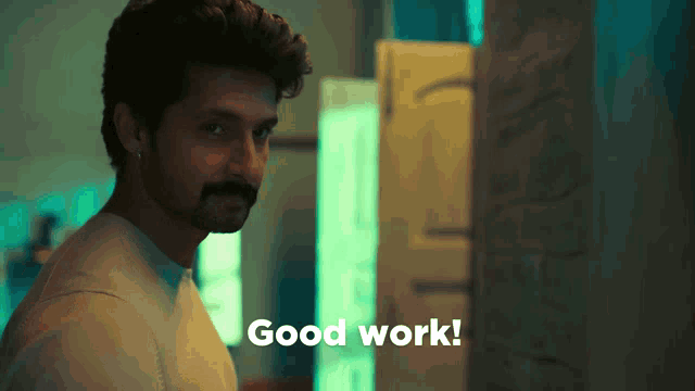 a man with a beard is standing in front of a sign that says good work