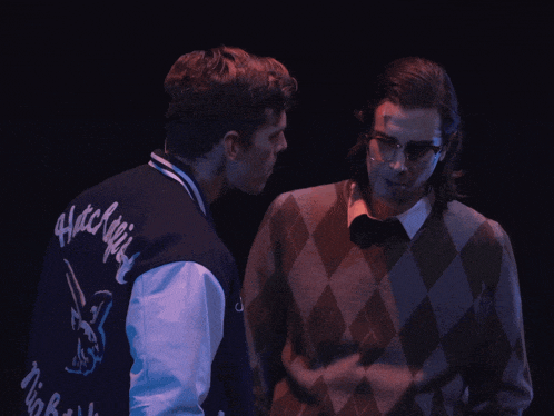 two men are looking at each other with one wearing a jacket that says ' hatchlin ' on it