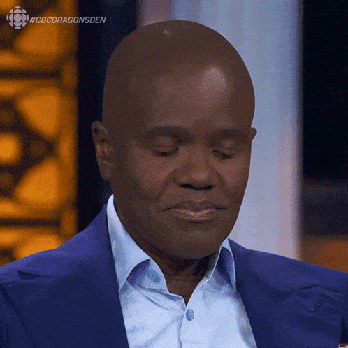 a bald man in a blue suit and white shirt with #cbcdragonsden written on the bottom